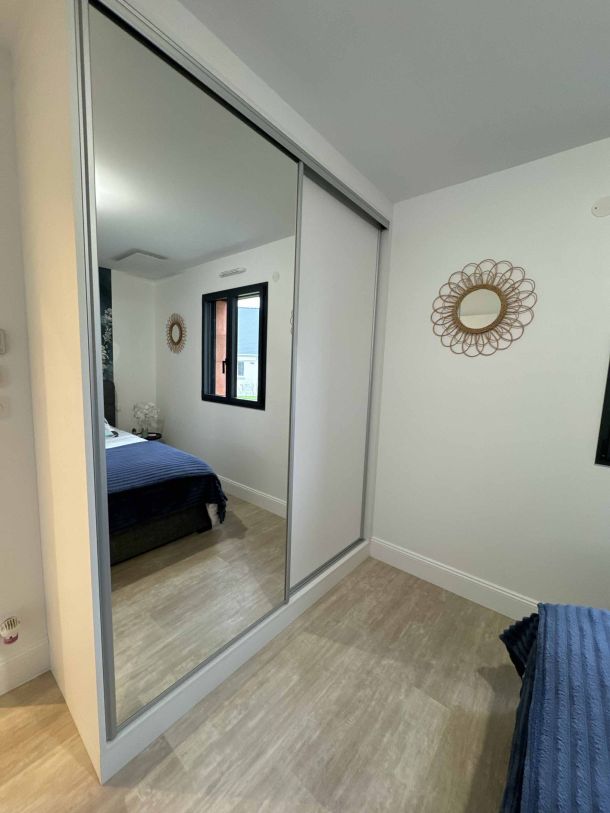 Placard avec portes coulissantes, dont une avec miroir, dans une chambre lumineuse au style moderne avec des détails décoratifs muraux et un sol en parquet clair."